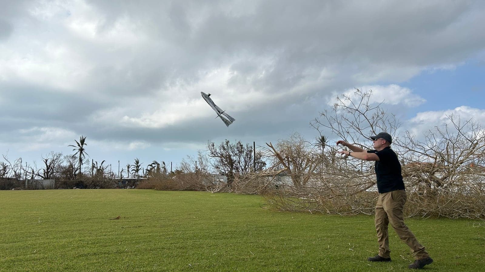 DOE field operator hand-launching a fixed-wing mapping drone among storm-damaged trees on Saipan